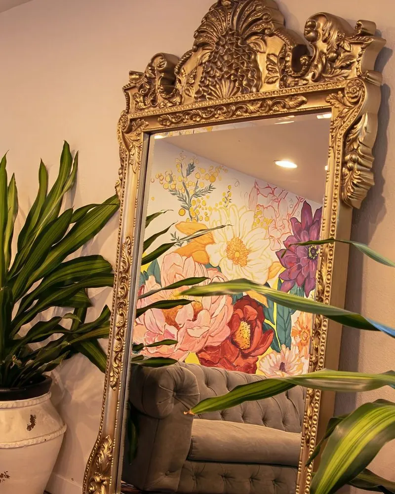 A gilded floor mirror at Wax &amp; Lash Berkeley reflecting the hand painted floral mural