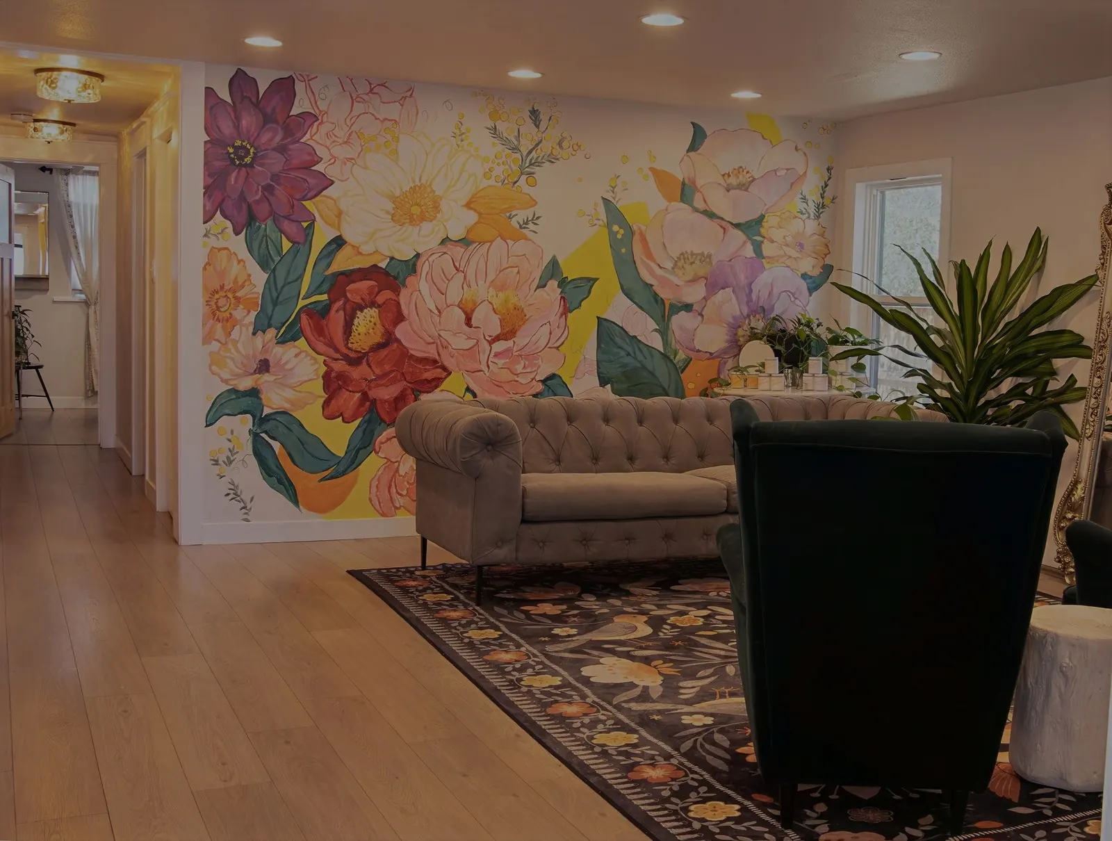 The lounge at Wax &amp; Lash Berkeley with a hand painted floral mural, a tufted sofa and velvet chairs