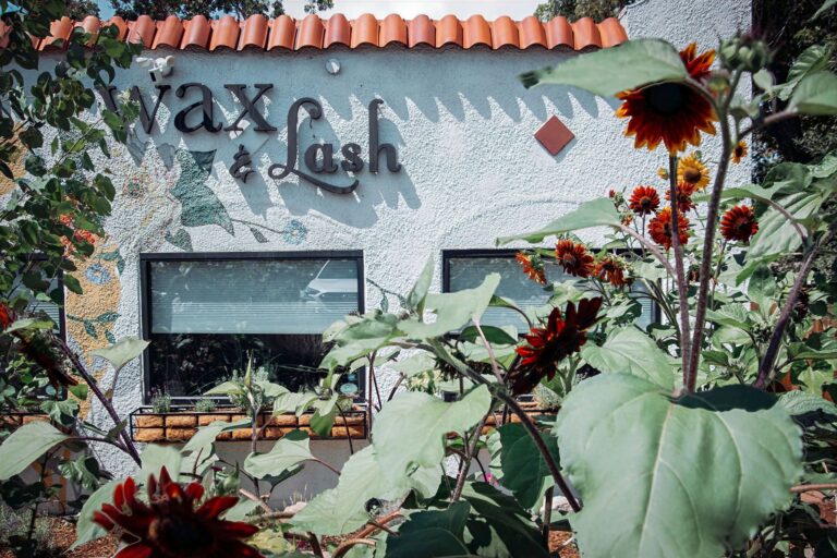 The Wax & Lash sign on the Berkeley studio in Denver framed by red sunflowers