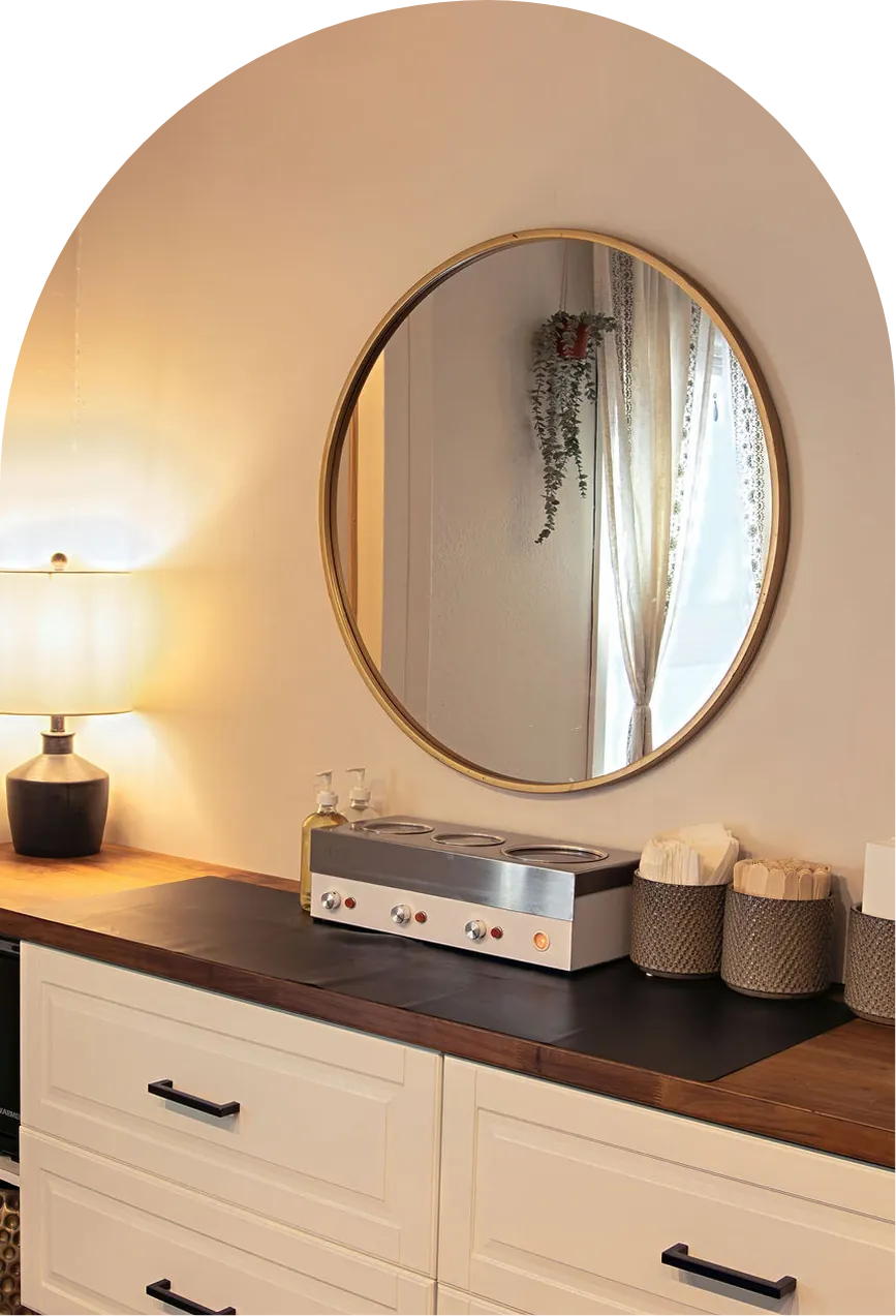 The brow station at Wax &amp; Lash, with a round gold mirror, soft lamp light and a wax warmer